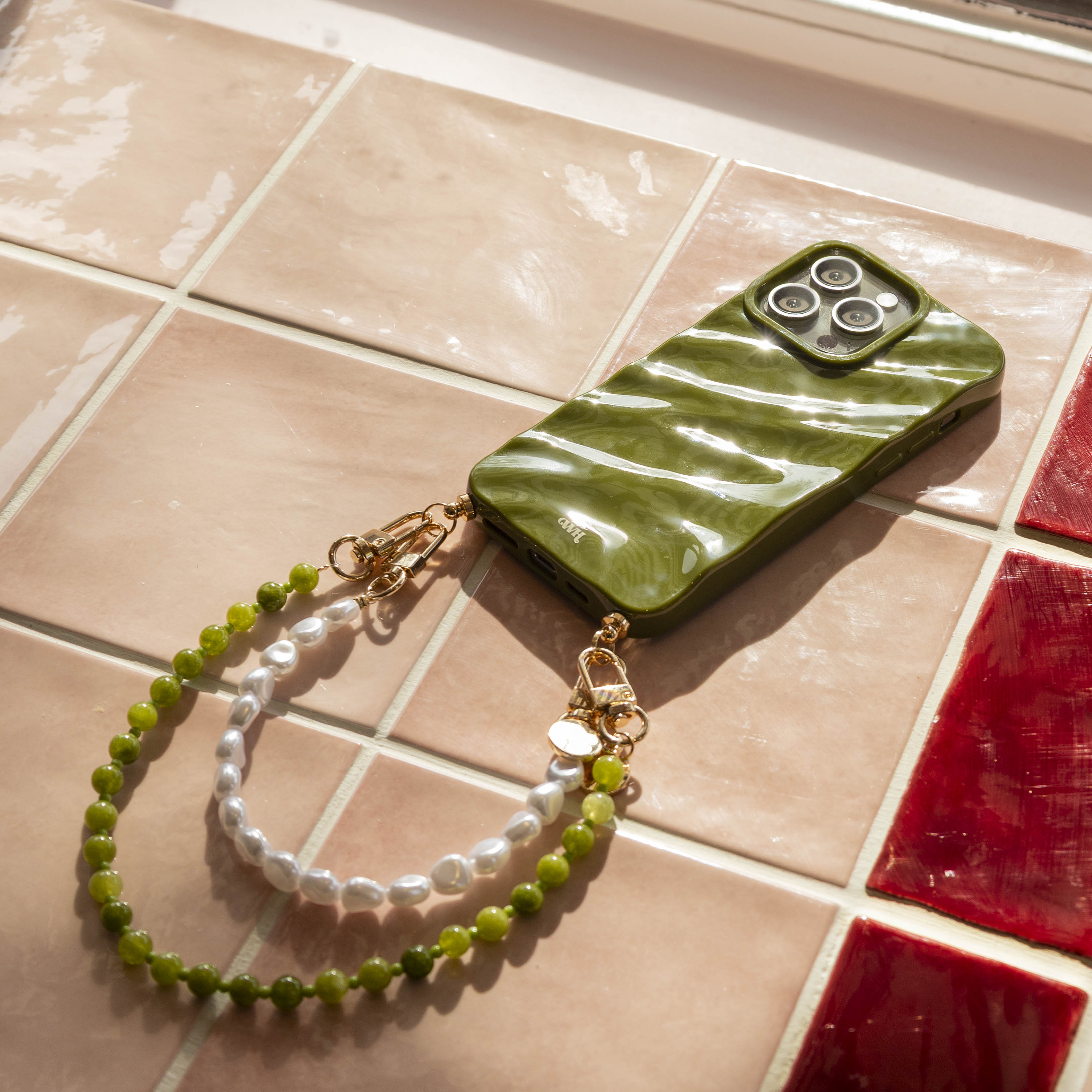 Glanzend donkergroen iPhone 11 hoesje met golvend design, bevestigd aan een kort groen kralenkoord en een wit parelkoord.