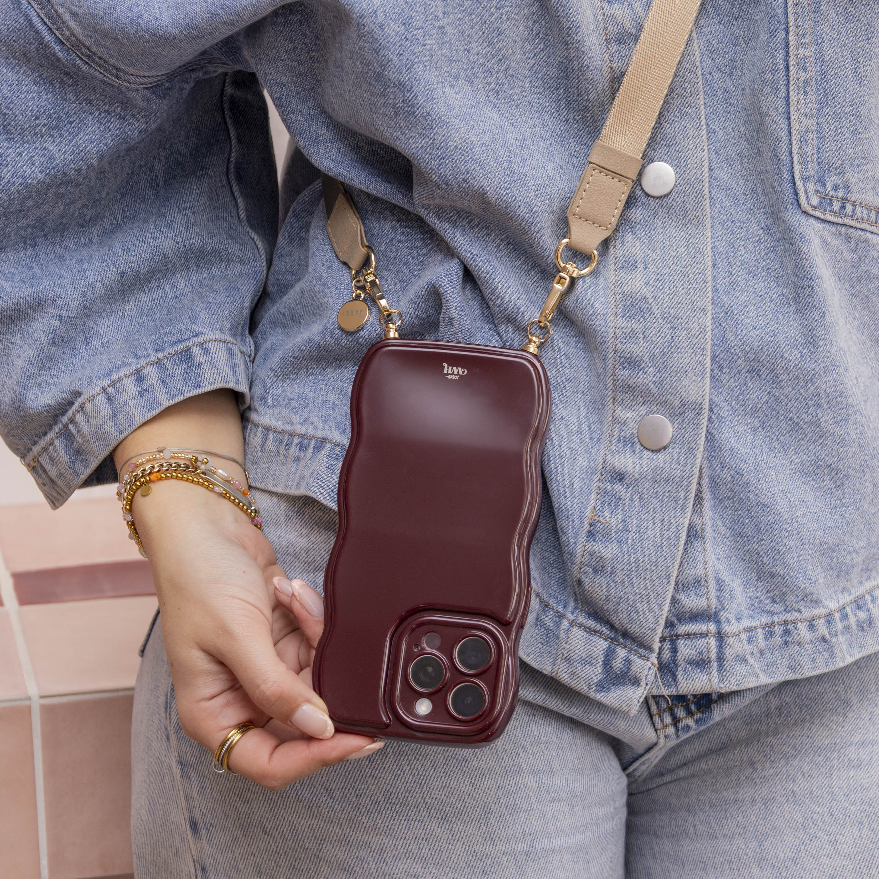 Beige lanyard strap met gouden clips, gedragen over een spijkerjasje, met een bordeauxrode telefoonhoes.