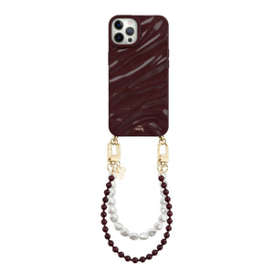Burgundy Glaze Cord iPhone 12 Pro Max case with shiny wavy texture, gold hardware, and pearl wrist strap.