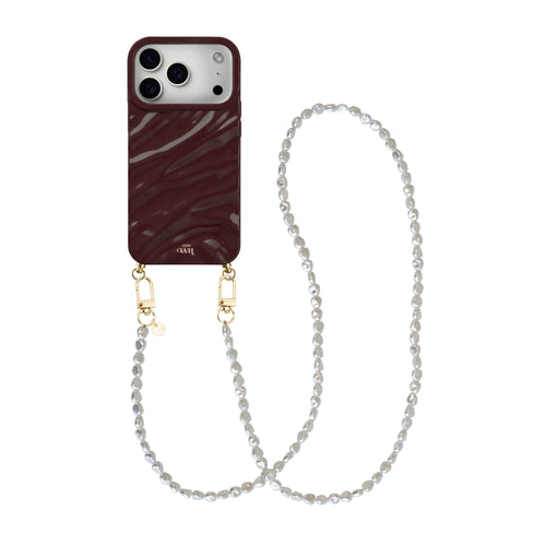 Bordeauxrode iPhone 17 Pro hoes met glanzende, golvende textuur en lang parelkoord met gouden details.