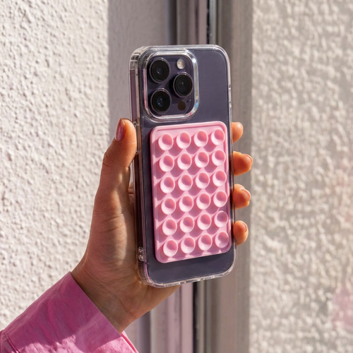 Hand houdt een paarse iPhone vast met een transparant hoesje en een vierkante roze zuignap sticker.