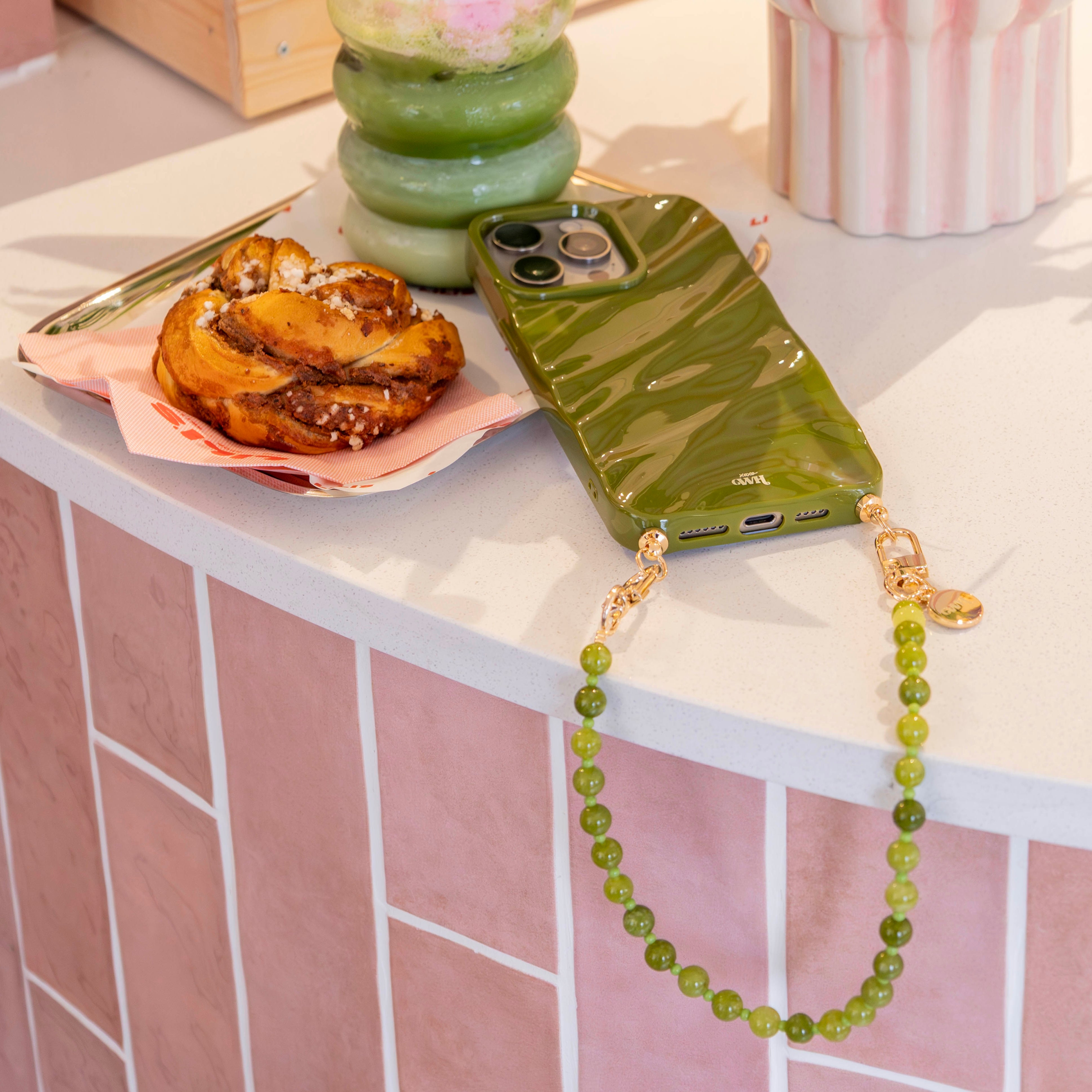 Glanzende groene iPhone 12 Glaze Cord Case met een bijpassende kralenketting en een kaneelbroodje.