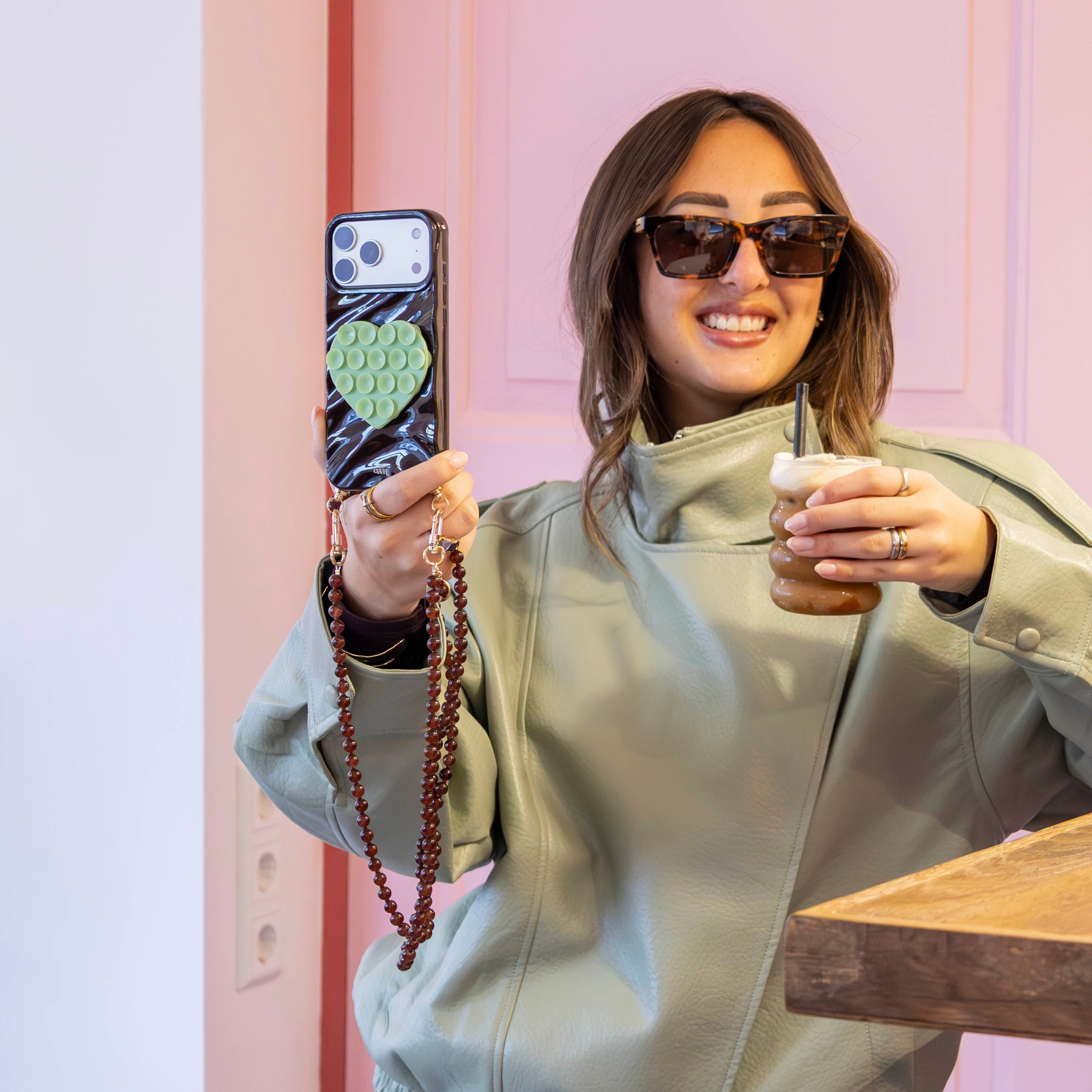 Smiling woman in sunglasses holding an iPhone 11 with a brown Glaze Cord Case and a matching long Brown Sugar cord.