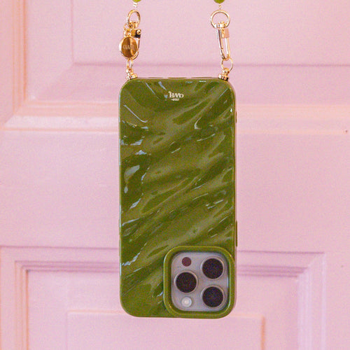 Glanzende groene iPhone 17 Pro hoes met marmerlook en gouden accenten, hangend aan een roze deur.