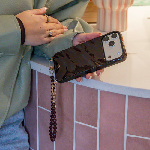 Hand holds a glossy brown iPhone 12 Pro Glaze Cord Case with a beaded Brown Sugar wrist strap.