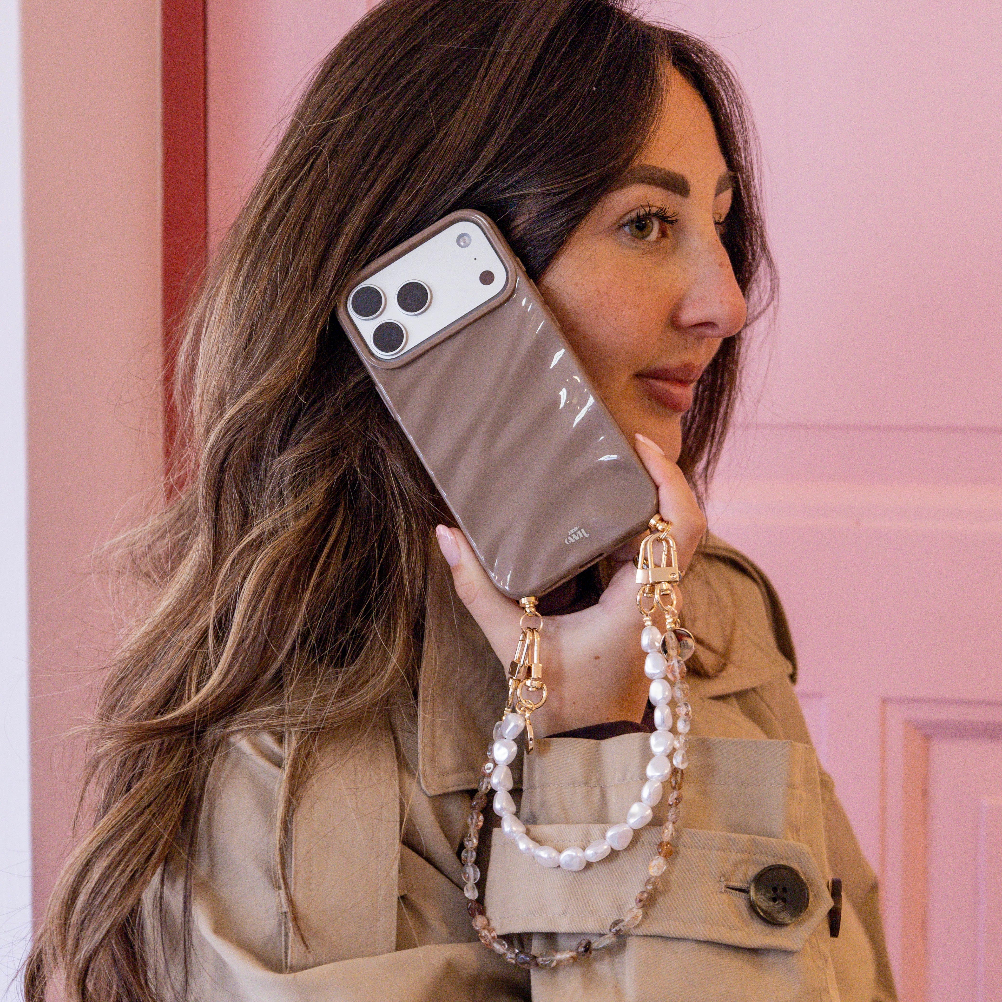 Vrouw met iPhone 13 Pro Max in glanzend taupe Glaze Cord Case met parelkoord.