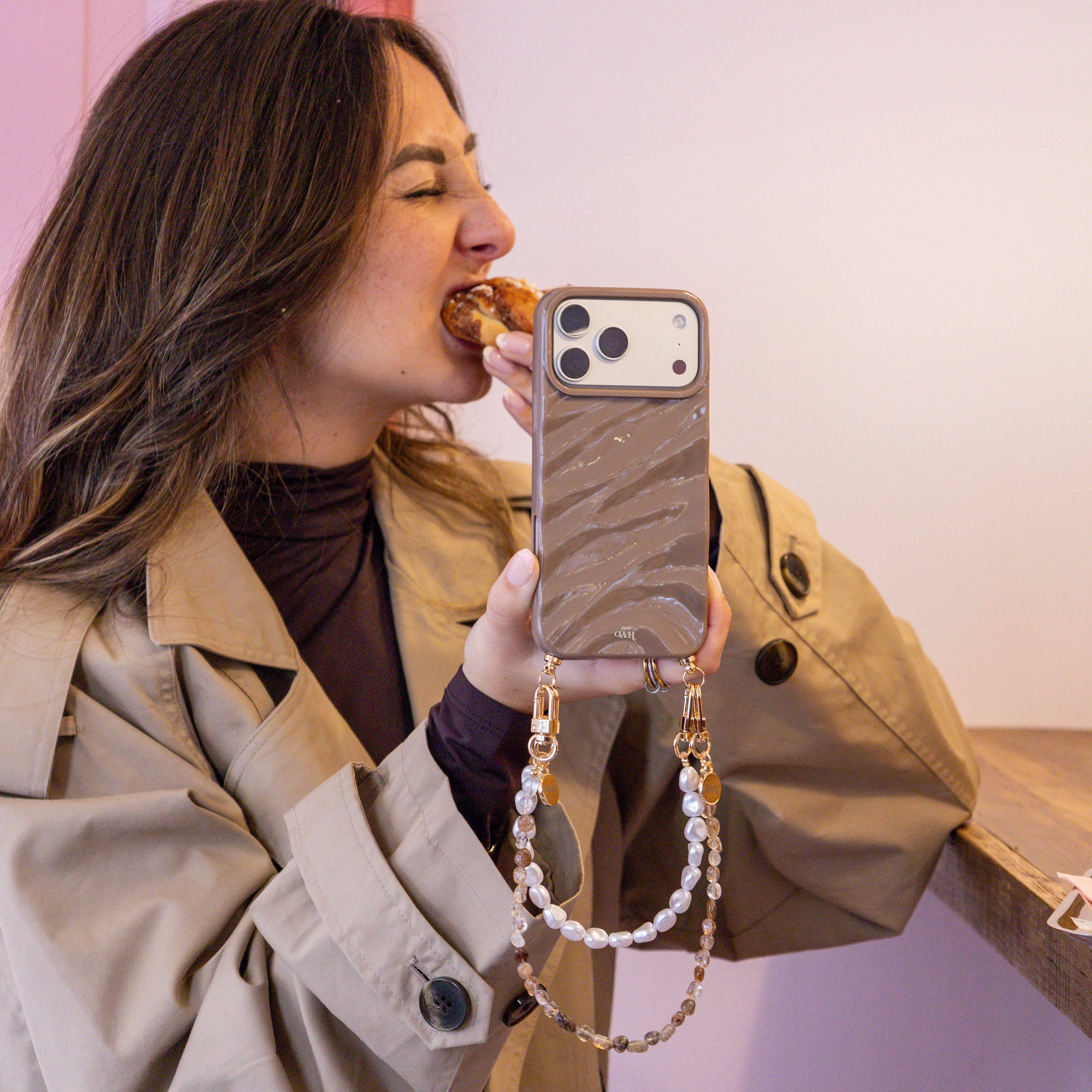 Vrouw met iPhone 17 Pro Max in taupe Glaze Cord Case met parelkoord en Soft Taupe koord.