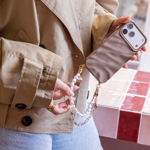 Glanzend taupe telefoonhoesje met golvend design, vastgehouden met een kort parelkoord en gouden accenten.