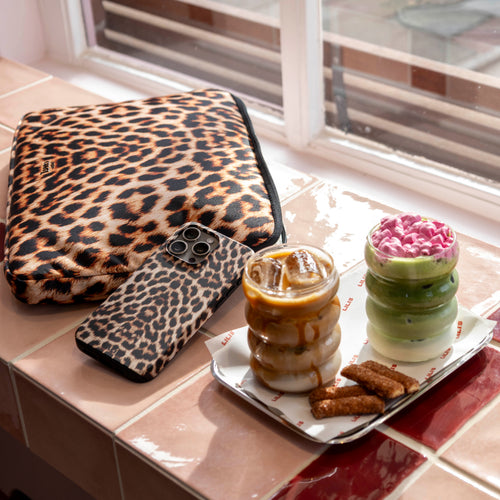 Leopard print "Wild Thing" double-layer phone case and matching laptop sleeve next to iced drinks.