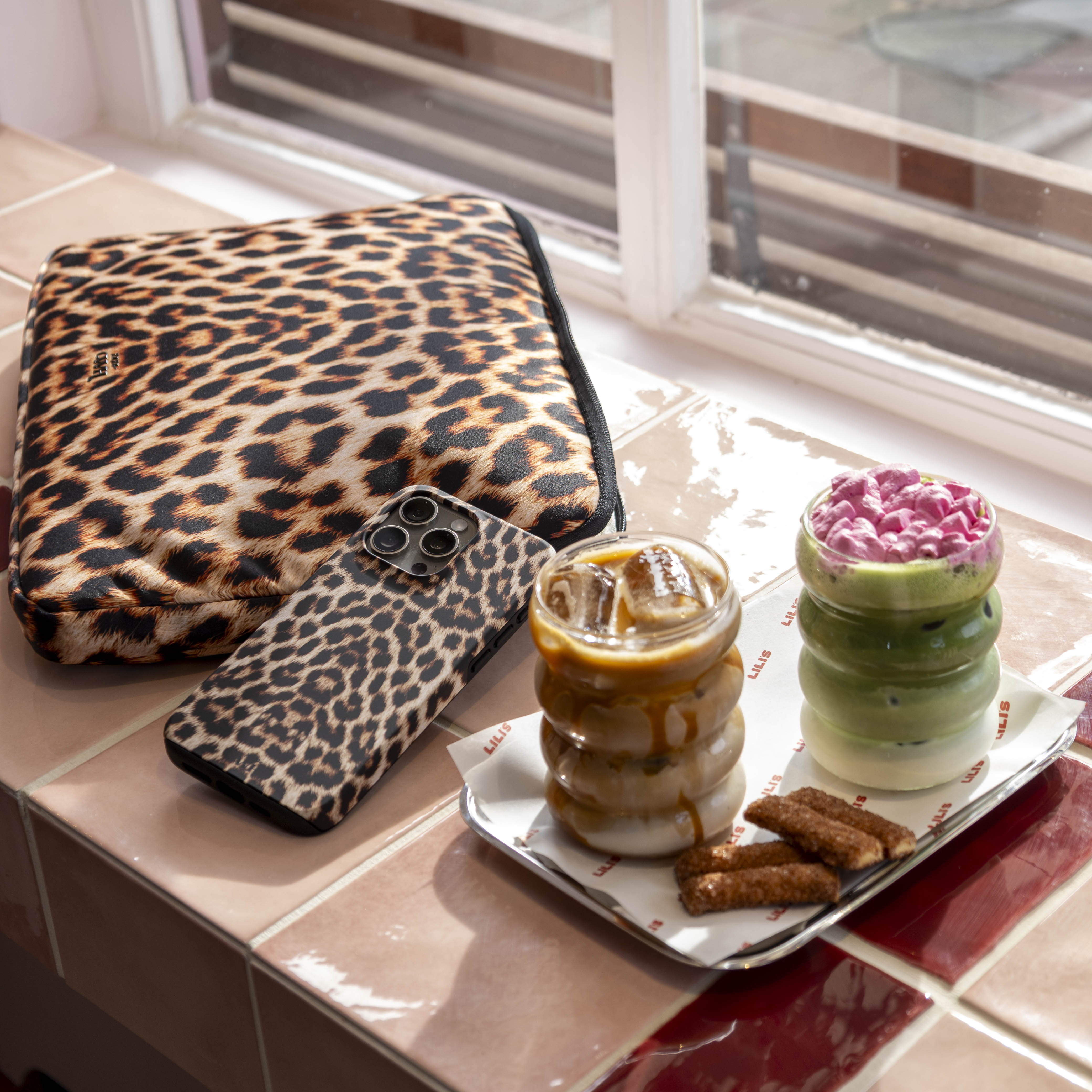 Leopard print "Wild Thing" double-layer phone case and matching laptop sleeve next to iced drinks.