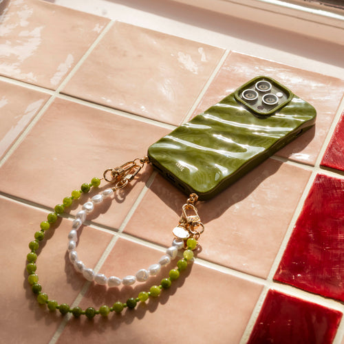 Glanzend donkergroen iPhone 11 hoesje met golvend design, bevestigd aan een kort groen kralenkoord en een wit parelkoord.