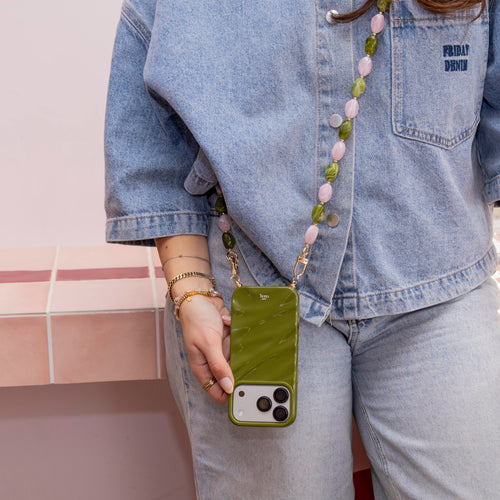 Groene glanzende iPhone 13 Pro hoes met lang Rose Quartz kralenkoord, gedragen door een persoon.