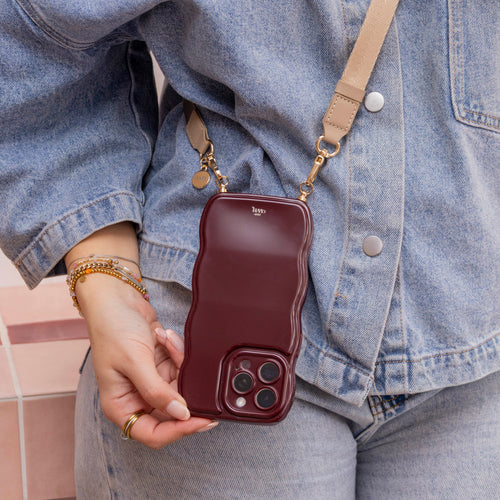 Beige lanyard strap met gouden clips, gedragen over een spijkerjasje, met een bordeauxrode telefoonhoes.