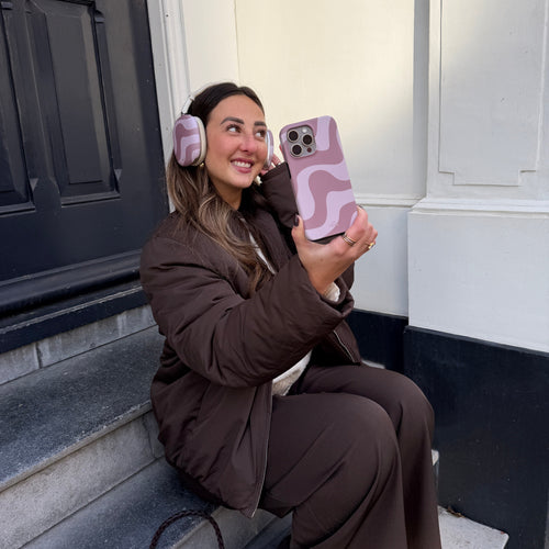 Vrolijke vrouw met AirPods Max covers in "Ride With Me Brown" en bijpassend telefoonhoesje.