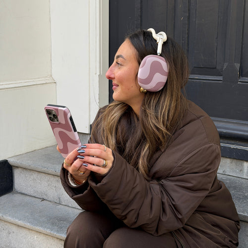 Vrouw draagt AirPods Max met roze-bruine golvende "Ride With Me Brown" covers en bijpassend telefoonhoesje.