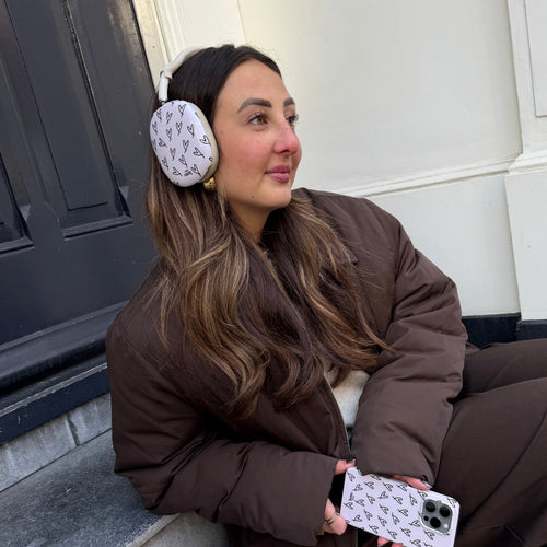 Vrouw draagt witte AirPods Max met zwarte hartjes covers, passend bij haar telefoonhoesje.