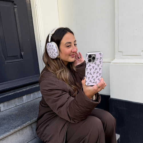 Vrouw met witte AirPods Max met hartjescovers en een bijpassend lila telefoonhoesje met hartjes.