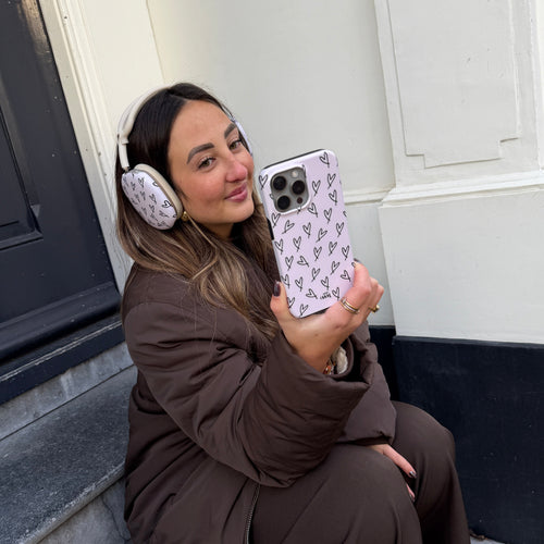Vrouw met AirPods Max met witte covers met zwarte hartjes en bijpassend telefoonhoesje.