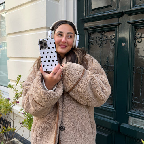 Vrouw met AirPods Max Polka Dots (Wit) covers en bijpassend telefoonhoesje, draagt een beige teddy jas.