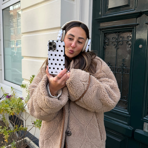 Vrouw met AirPods Max Polka Dots (Wit) covers en bijpassend telefoonhoesje, draagt een teddy jas.