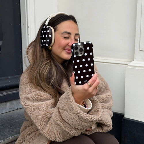 Vrouw met AirPods Max met zwarte polka dot covers en bijpassend telefoonhoesje, zittend op een stoep.