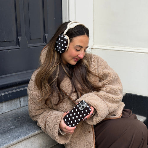 Vrouw draagt AirPods Max met zwarte polka dot covers en bijpassend telefoonhoesje, zittend op een stoep.