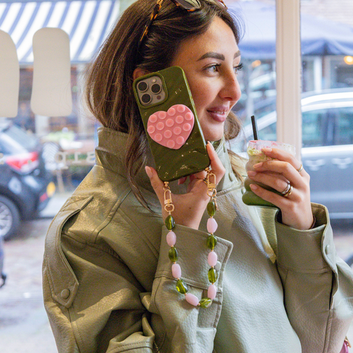 Vrouw met groene telefoonhoes, roze hart popsocket en korte Rose Quartz polsband met roze en groene kralen.