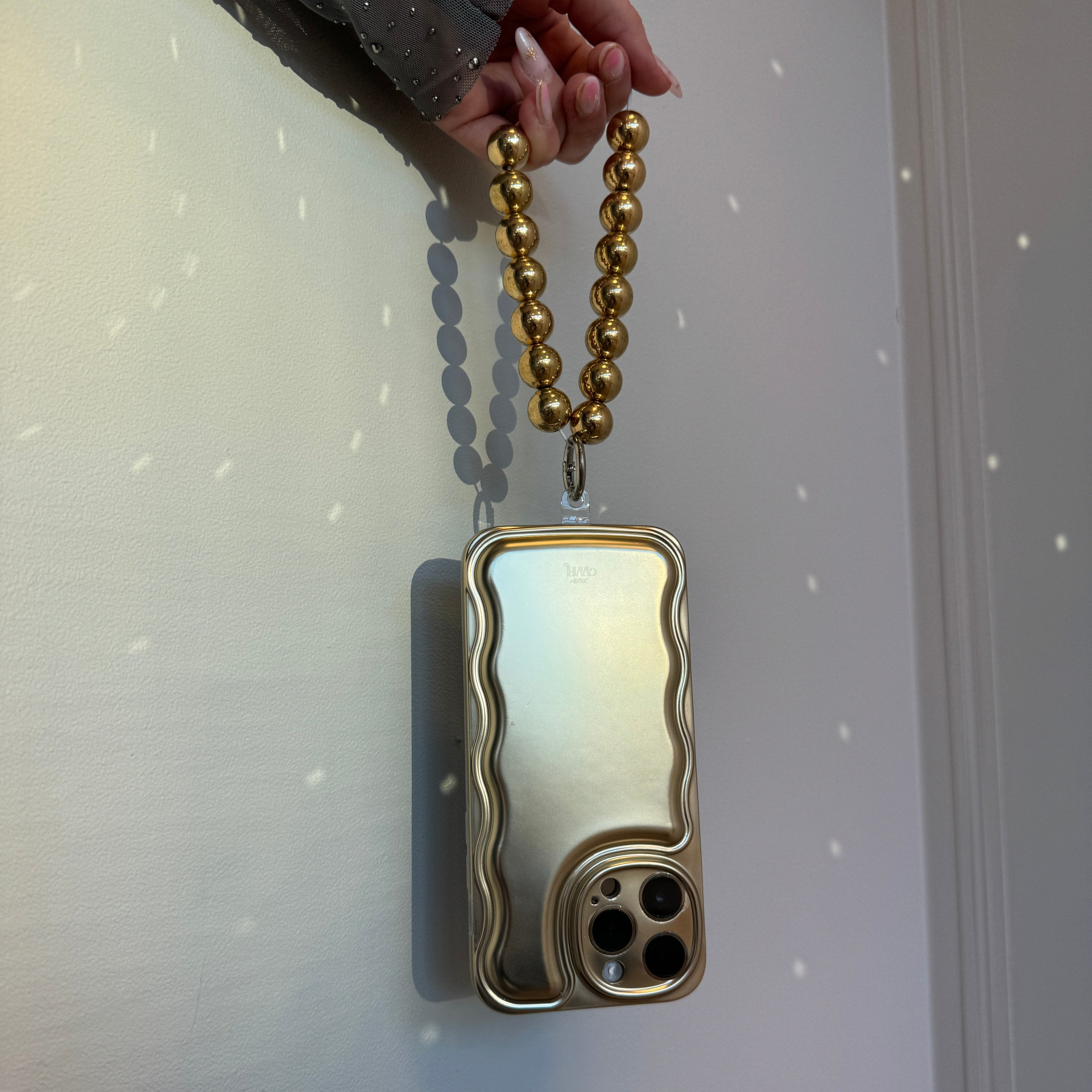 Hand holding a shiny gold iPhone case with a wavy design and a chunky gold beaded easy cord.